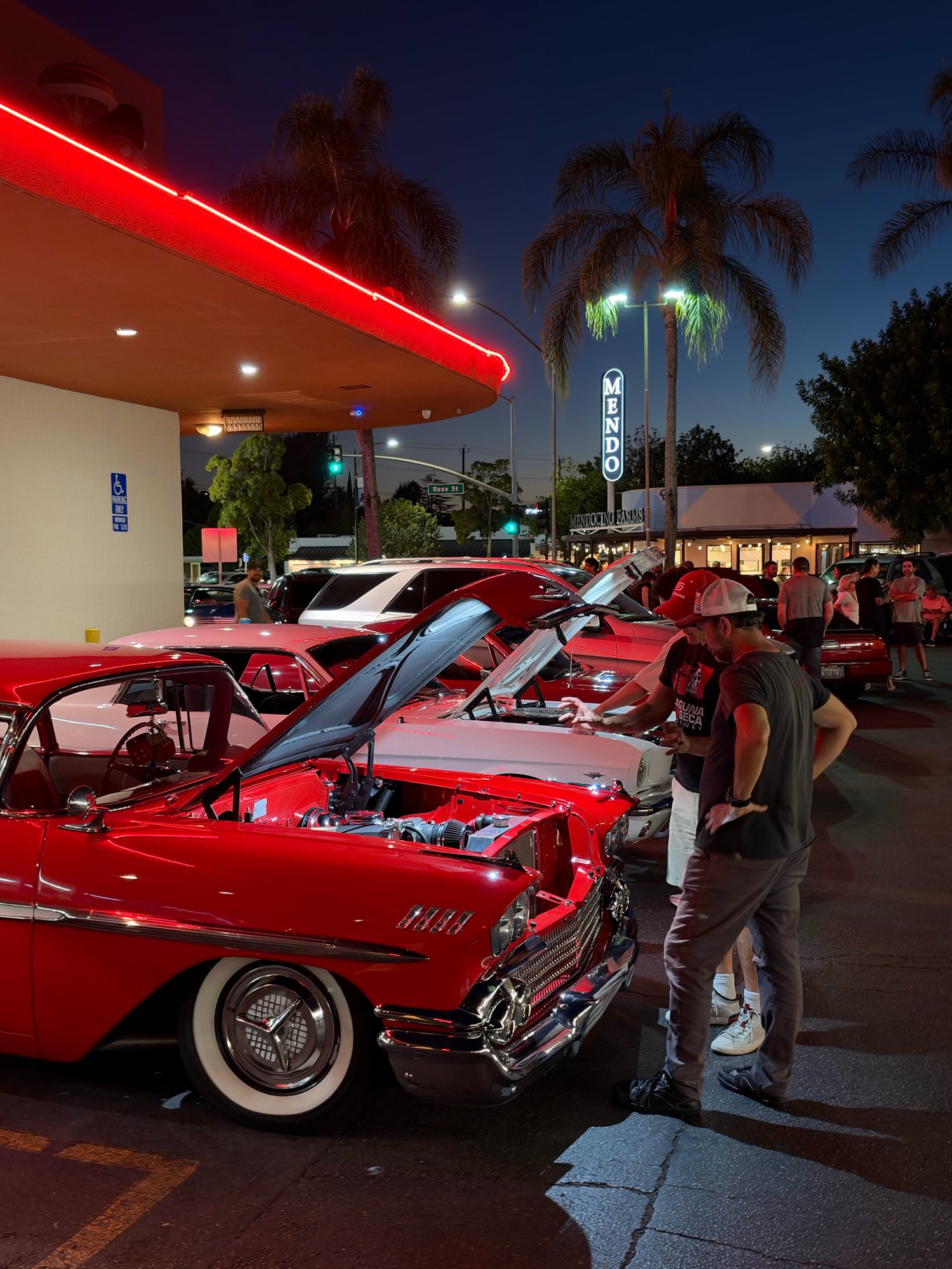 Red 1958 Chevy Impala with hood open at Bob's Big Boy Burbank car night, under red neon with palm trees