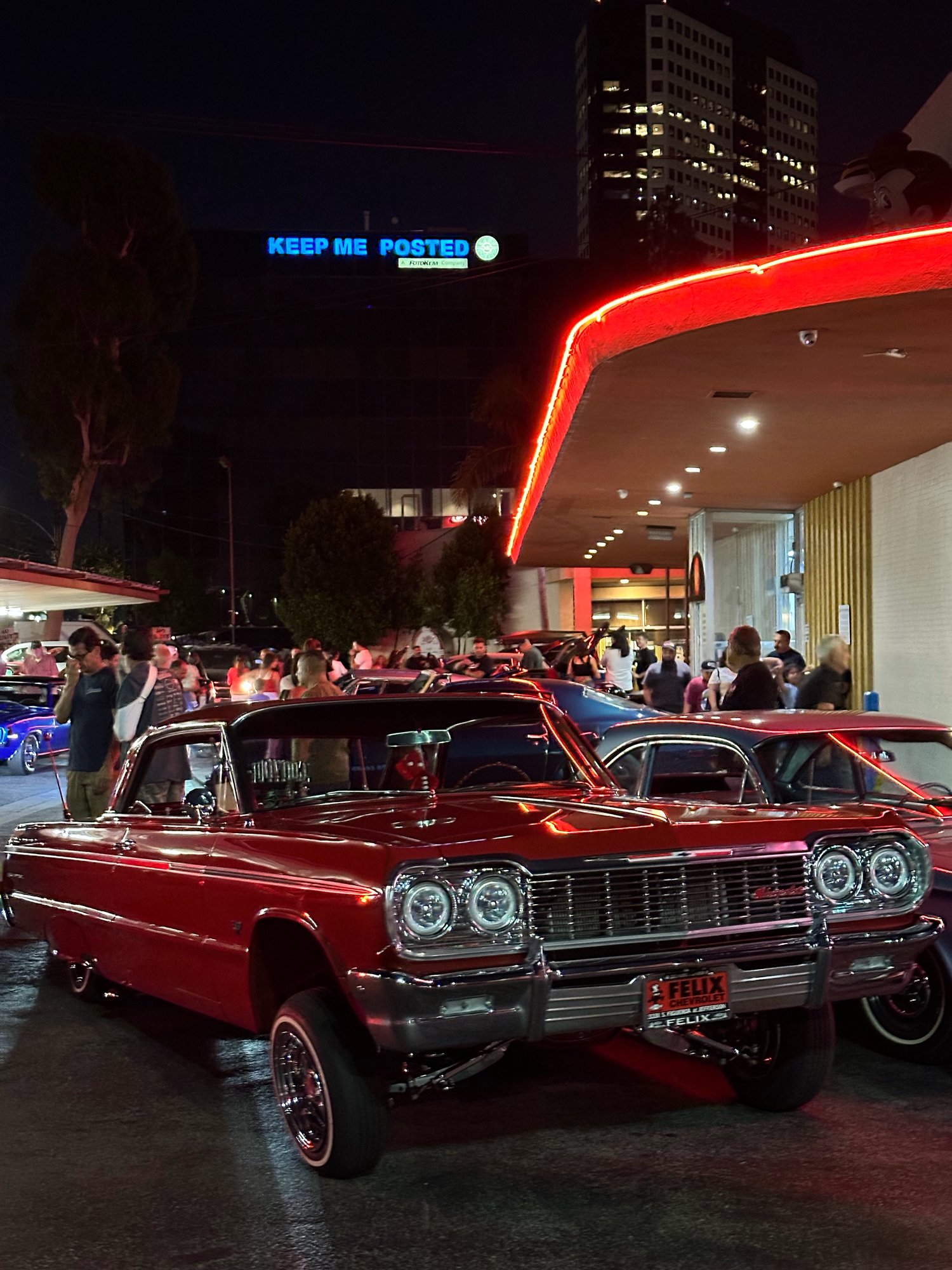 Red 1964 Impala lowrider under red neon at Bob's Big Boy Burbank car night with a crowd